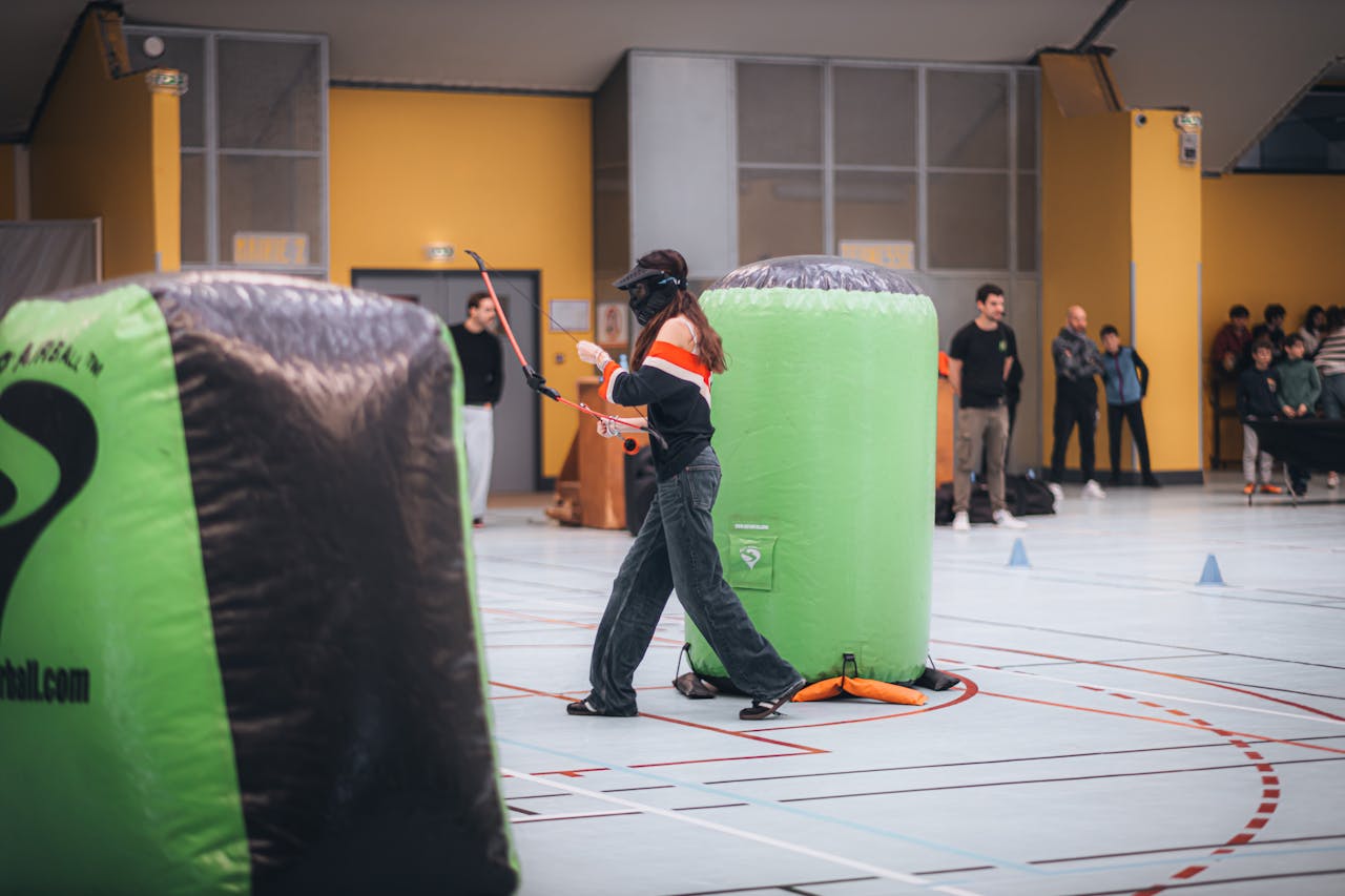 A woman playing archery tag indoors, navigating around obstacles and aiming.