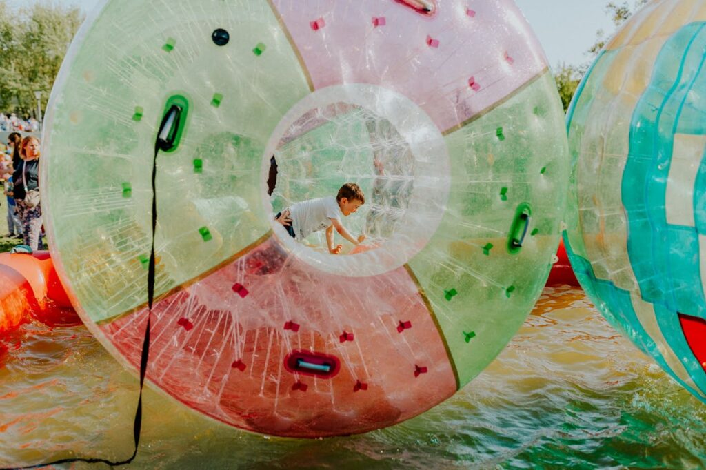 A child enjoys playing inside a vibrant inflatable water ball at an outdoor fair.